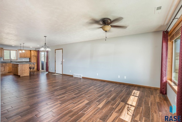 unfurnished living room with a textured ceiling, ceiling fan with notable chandelier, a sink, visible vents, and dark wood finished floors