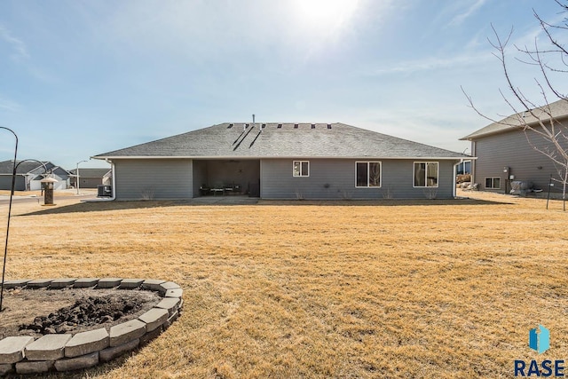 rear view of property with a shingled roof and a lawn