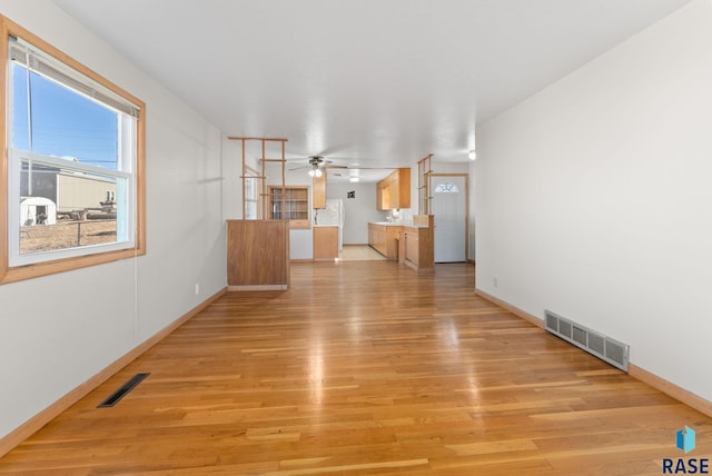 unfurnished living room with ceiling fan, light wood-style flooring, visible vents, and baseboards