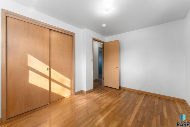 unfurnished bedroom featuring hardwood / wood-style flooring, baseboards, and a closet