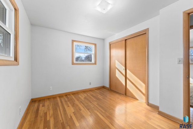 unfurnished bedroom featuring light wood finished floors, baseboards, and a closet