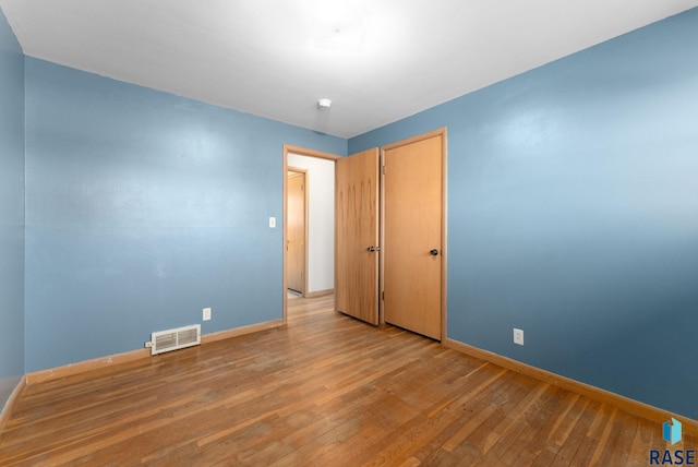 empty room featuring hardwood / wood-style flooring, visible vents, and baseboards