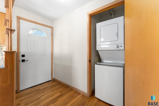 laundry room with laundry area, stacked washer / dryer, light wood-style flooring, and baseboards