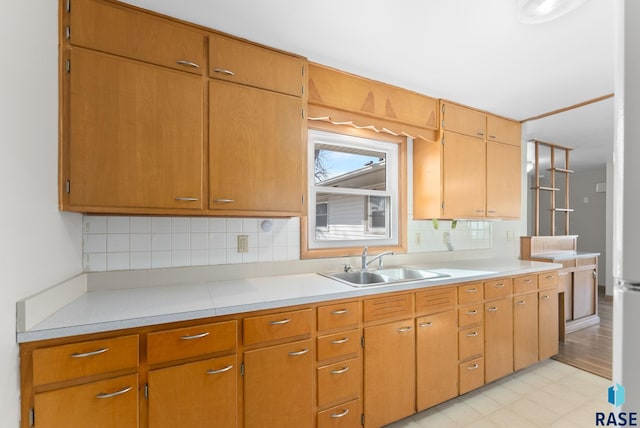 kitchen with brown cabinetry, decorative backsplash, light countertops, light floors, and a sink