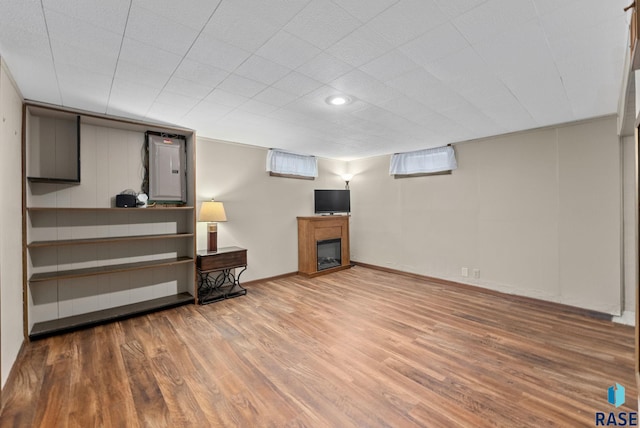 basement featuring baseboards, wood finished floors, and a glass covered fireplace