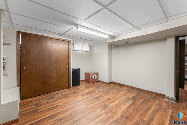 finished basement featuring wood finished floors, a paneled ceiling, and baseboards