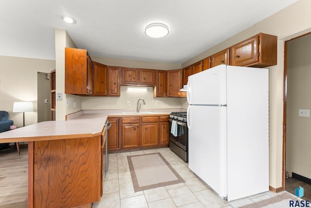 kitchen featuring a peninsula, a sink, light countertops, freestanding refrigerator, and stainless steel range with gas stovetop