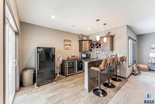 kitchen with beverage cooler, dark countertops, decorative light fixtures, a peninsula, and freestanding refrigerator