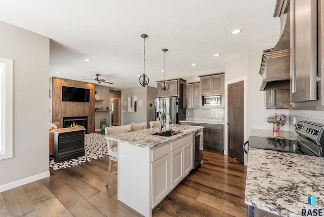 kitchen featuring stainless steel appliances, a fireplace, a sink, hanging light fixtures, and a center island with sink