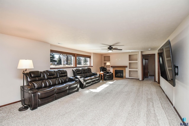 living area with ceiling fan, baseboards, a glass covered fireplace, and light colored carpet