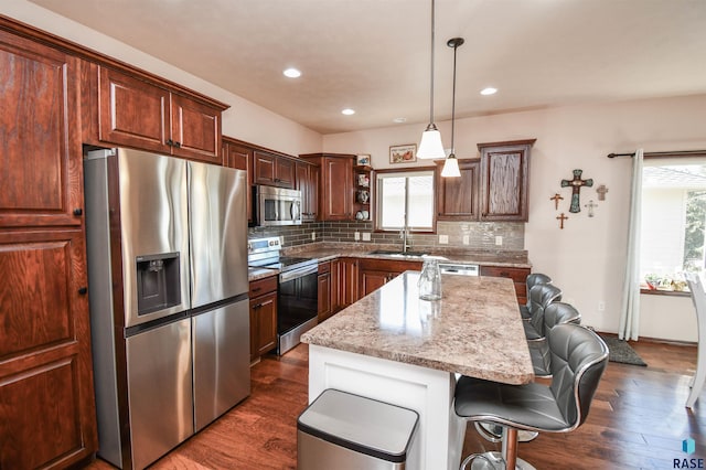 kitchen featuring light stone counters, pendant lighting, stainless steel appliances, a sink, and a kitchen island