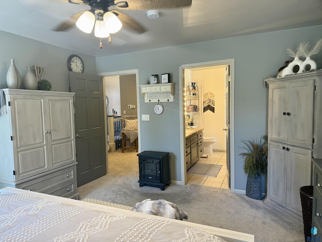 bedroom with light tile patterned flooring, connected bathroom, light colored carpet, a ceiling fan, and a wood stove