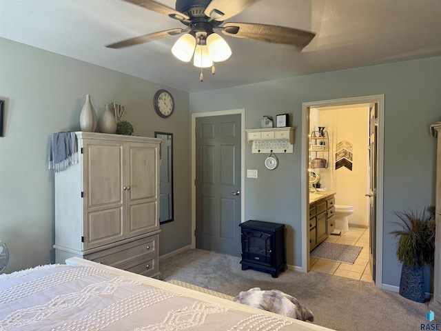 bedroom with light tile patterned floors, connected bathroom, light colored carpet, a ceiling fan, and a wood stove