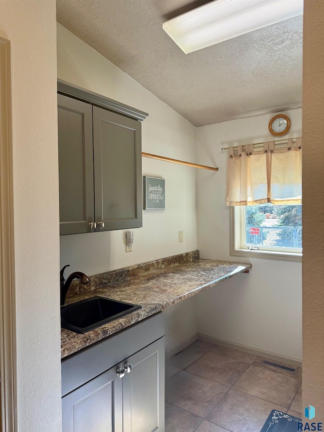 kitchen with gray cabinets, visible vents, light tile patterned flooring, a sink, and a textured ceiling