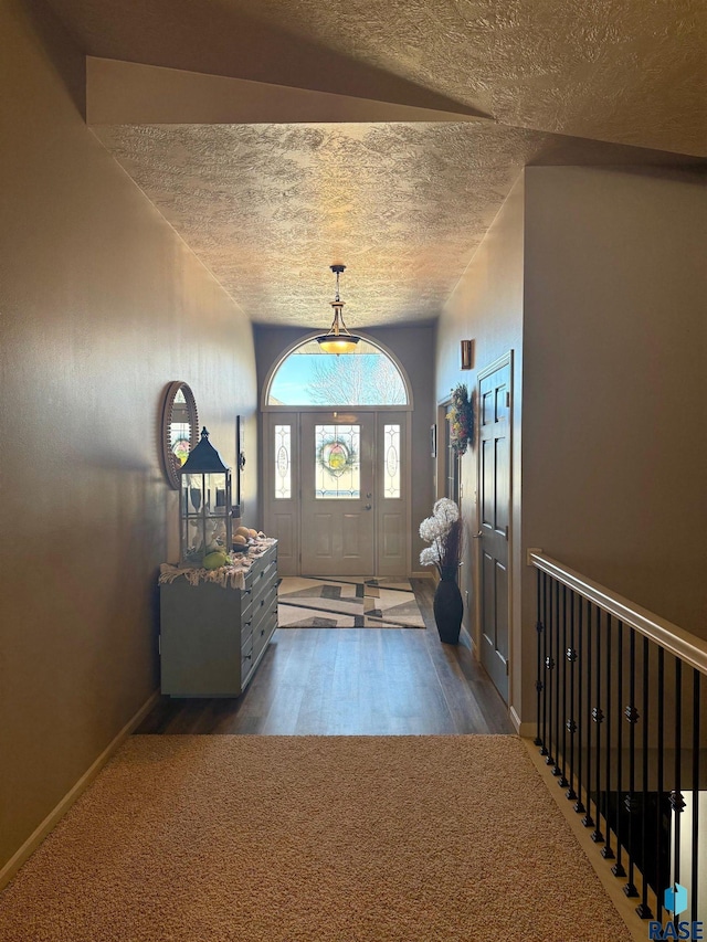 entryway with a textured ceiling, dark colored carpet, and baseboards