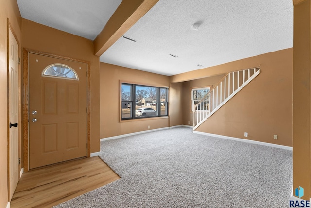 carpeted entrance foyer featuring stairs, a textured ceiling, and baseboards