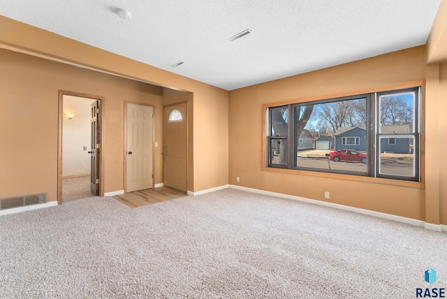 unfurnished room featuring light carpet, baseboards, visible vents, and a textured ceiling