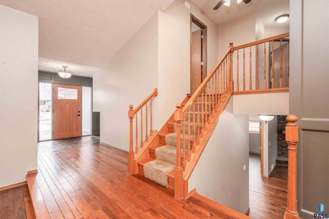 foyer entrance with ceiling fan, a towering ceiling, baseboards, stairway, and hardwood / wood-style floors