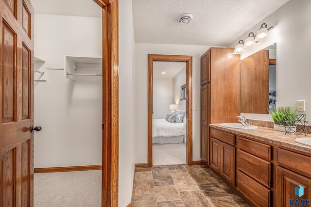 ensuite bathroom with double vanity, ensuite bath, a walk in closet, a textured ceiling, and a sink