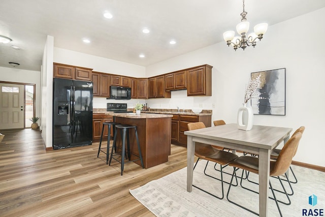 kitchen with pendant lighting, light countertops, light wood-style floors, a kitchen island, and black appliances