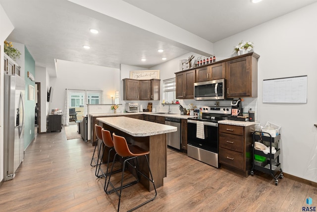 kitchen with light countertops, light wood-style flooring, appliances with stainless steel finishes, a sink, and dark brown cabinets