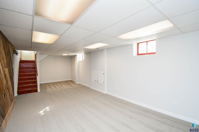 below grade area with carpet, stairs, baseboards, and a drop ceiling