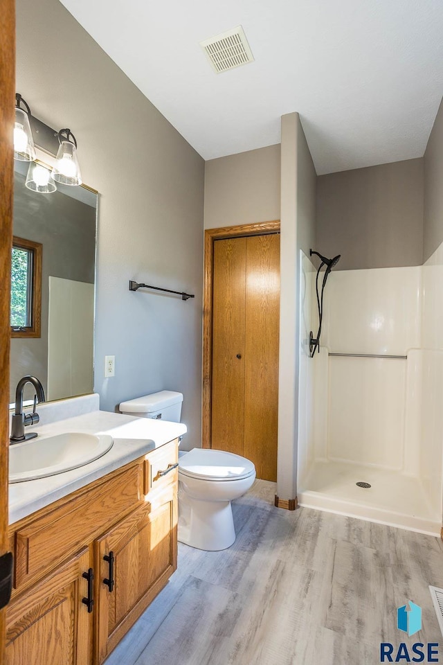 bathroom featuring toilet, wood finished floors, vanity, visible vents, and walk in shower