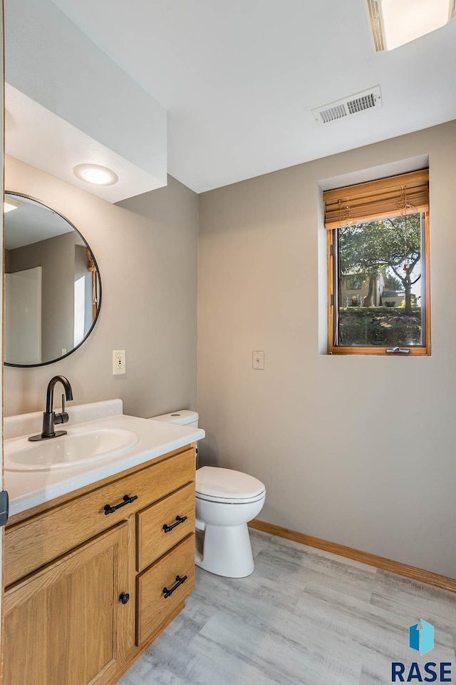 half bath featuring toilet, wood finished floors, vanity, visible vents, and baseboards