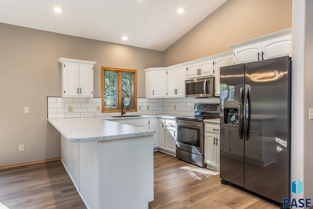 kitchen with white cabinets, lofted ceiling, a peninsula, stainless steel appliances, and a sink