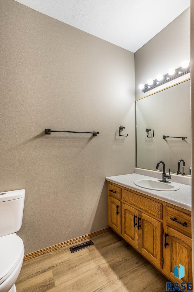 half bath with visible vents, baseboards, toilet, wood finished floors, and vanity