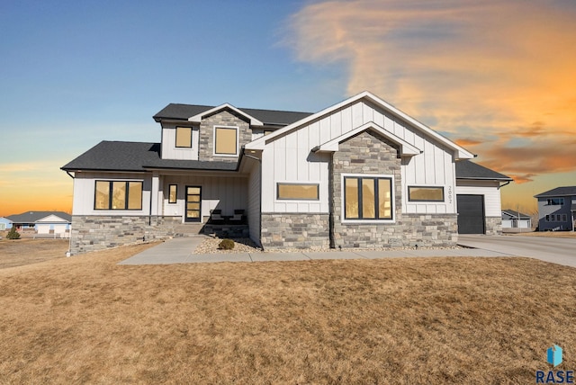 modern farmhouse style home with board and batten siding, stone siding, a yard, and an attached garage