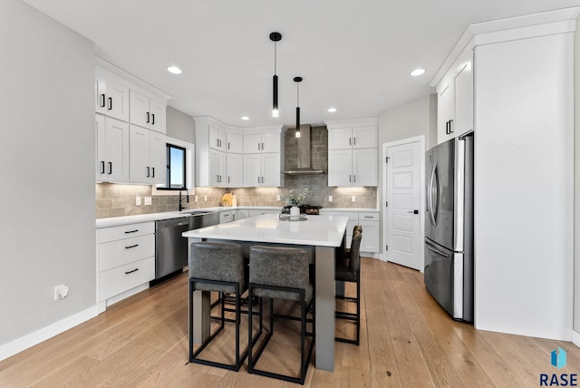 kitchen with light wood-style floors, appliances with stainless steel finishes, a breakfast bar, light countertops, and wall chimney range hood