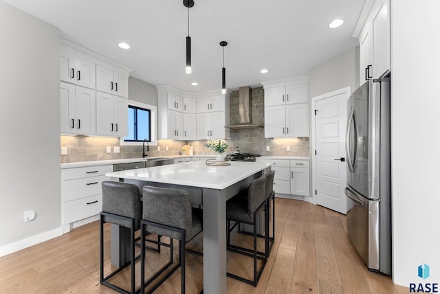 kitchen with light wood finished floors, freestanding refrigerator, a sink, wall chimney range hood, and a kitchen breakfast bar