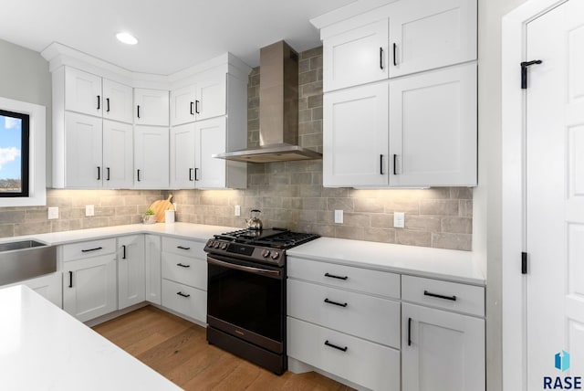 kitchen with light wood-style floors, light countertops, wall chimney range hood, backsplash, and gas range