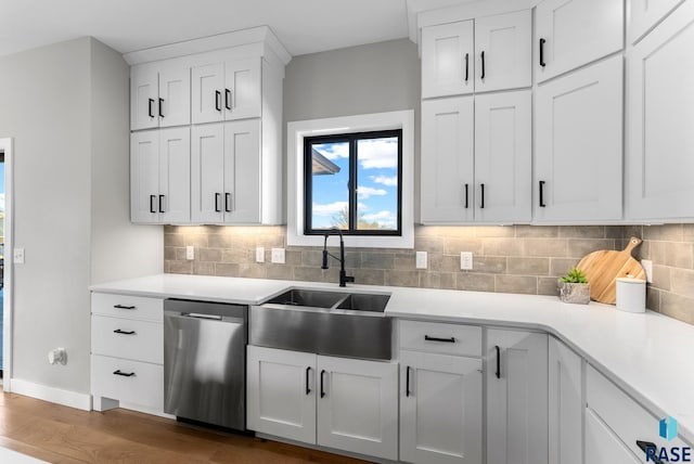 kitchen with decorative backsplash, white cabinets, dishwasher, light countertops, and a sink