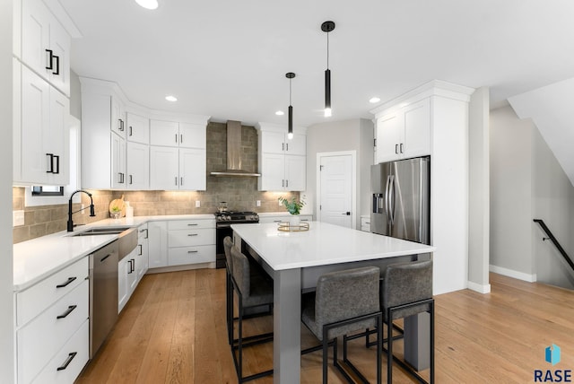 kitchen with a center island, appliances with stainless steel finishes, a sink, wall chimney range hood, and a kitchen breakfast bar