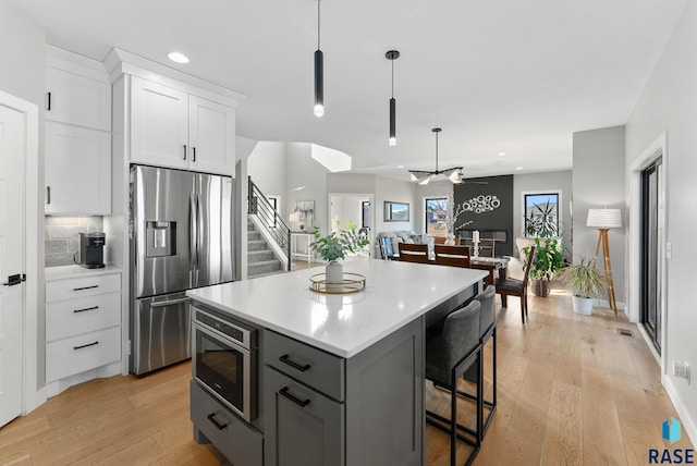 kitchen featuring white cabinets, stainless steel fridge with ice dispenser, a center island, built in microwave, and a kitchen bar