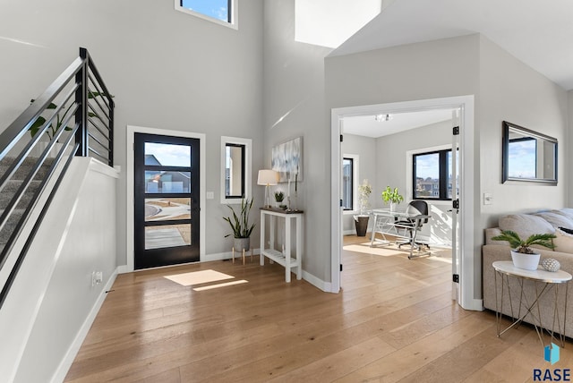 entryway with stairway, light wood-style flooring, a high ceiling, and baseboards