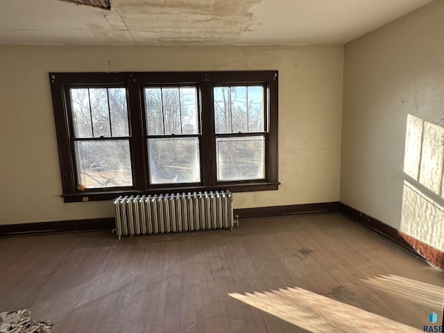 spare room featuring radiator, baseboards, and hardwood / wood-style floors