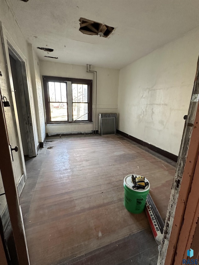 empty room featuring radiator, baseboards, and hardwood / wood-style floors