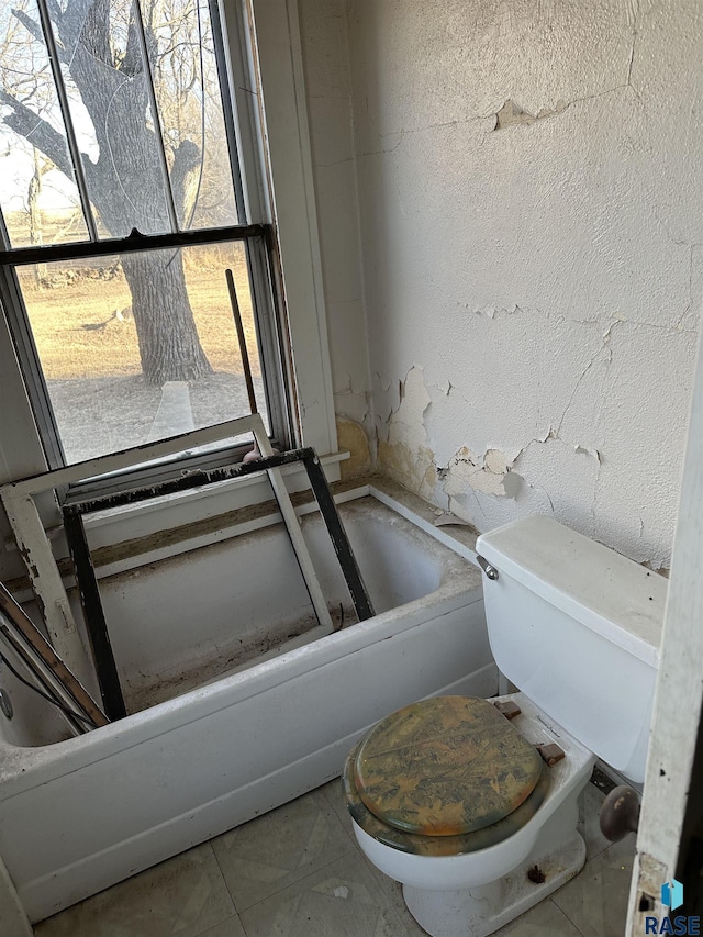 bathroom featuring toilet, a tub, tile patterned flooring, and a textured wall