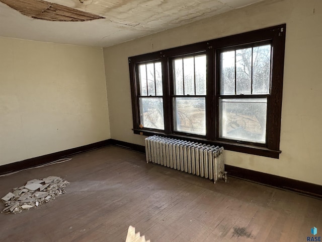 spare room with baseboards, hardwood / wood-style floors, and radiator heating unit