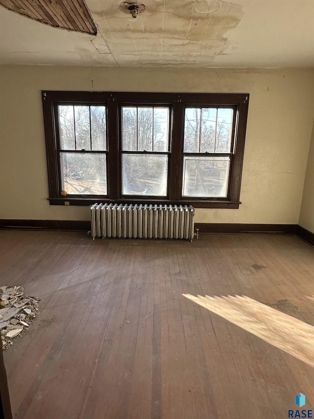 unfurnished room featuring radiator heating unit, plenty of natural light, wood-type flooring, and baseboards