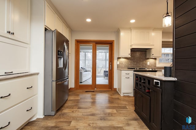 kitchen with tasteful backsplash, custom range hood, light wood-style floors, white cabinets, and stainless steel fridge with ice dispenser