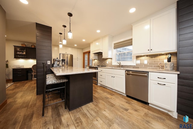 kitchen with appliances with stainless steel finishes, white cabinetry, light wood-style floors, and backsplash