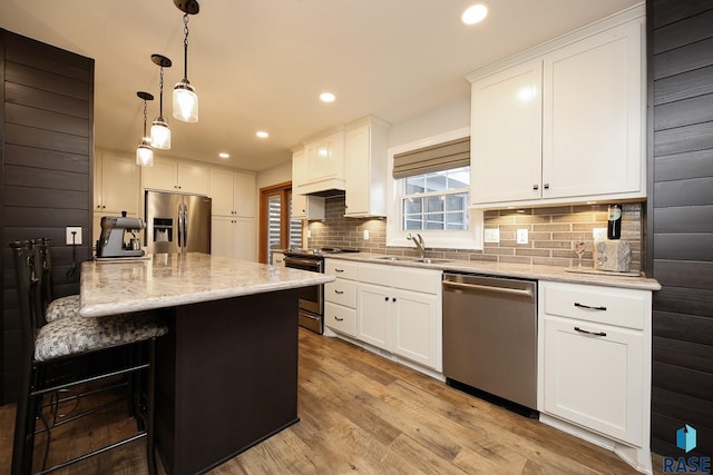 kitchen featuring tasteful backsplash, white cabinets, appliances with stainless steel finishes, light stone countertops, and light wood-type flooring