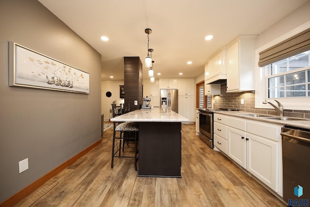 kitchen featuring backsplash, appliances with stainless steel finishes, white cabinets, a sink, and wood finished floors