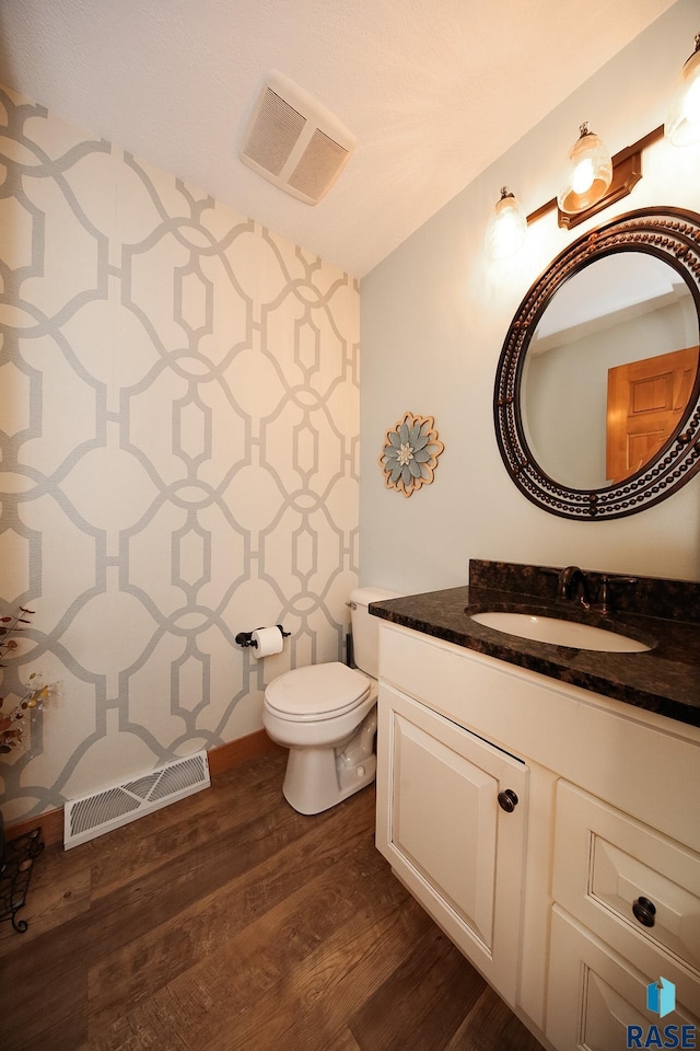 half bath featuring toilet, vanity, wood finished floors, and visible vents