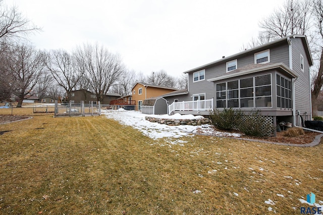 rear view of property featuring a lawn, a sunroom, an outbuilding, a storage unit, and fence