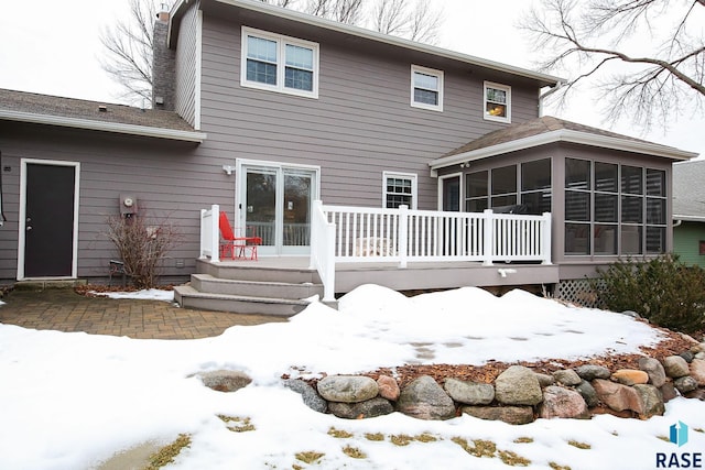 snow covered rear of property with a sunroom